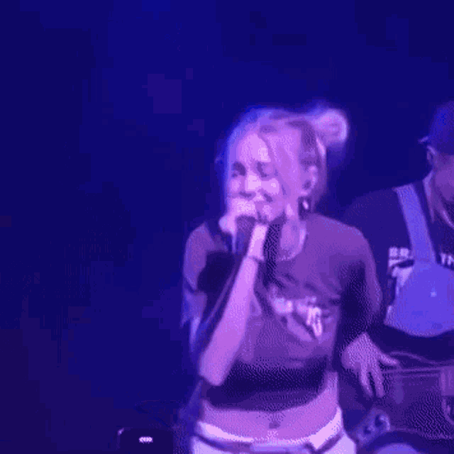 a woman is singing into a microphone on a stage with a man playing a guitar behind her .