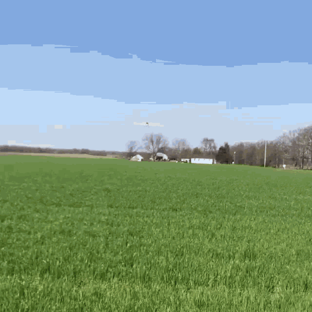 a plane is flying over a grassy field in the distance