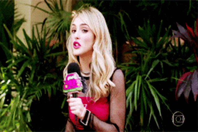 a woman in a red top is holding a microphone in front of plants