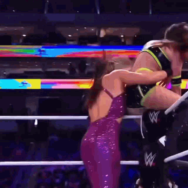 a woman in a purple dress is standing in a wrestling ring with a w logo on her leg .