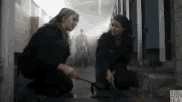 two women are kneeling in a hallway with a man in a wheelchair in the background .