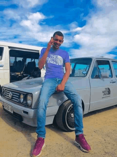 a man is sitting on the hood of a white car .