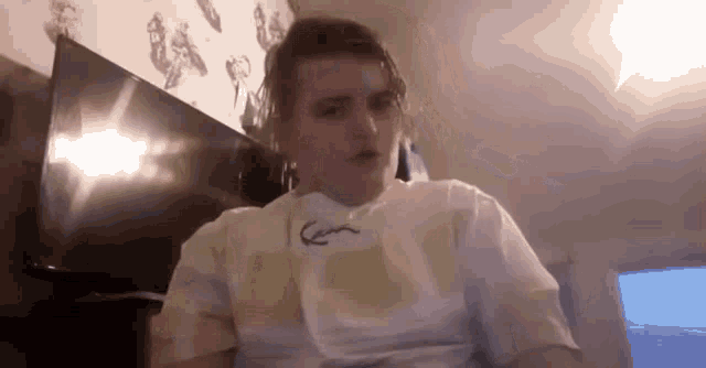 a young man wearing a white t-shirt is sitting in front of a television in a room .