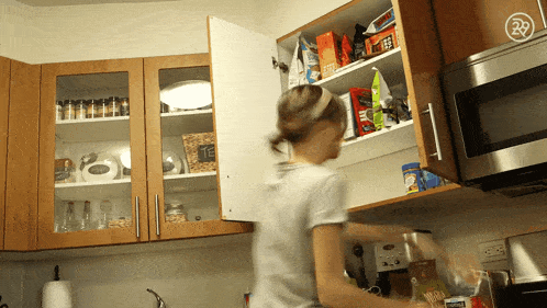 a woman in a kitchen reaches into a cupboard with a bag of nescafe coffee on the shelf
