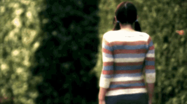 a woman wearing a striped sweater is walking in a park