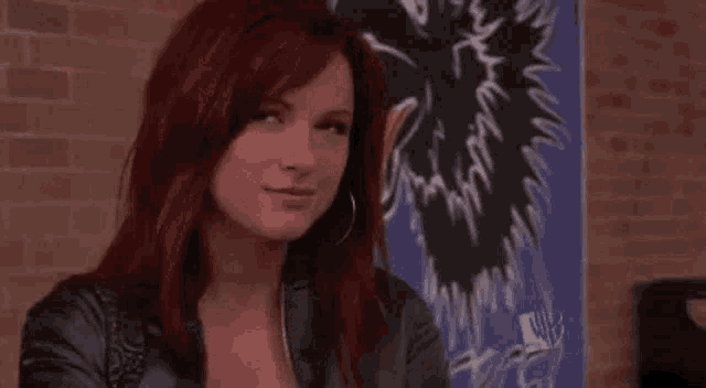 a woman with red hair is smiling in front of a brick wall in a room .