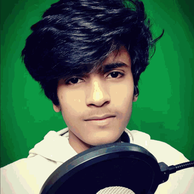 a young man holding a microphone with a green background behind him
