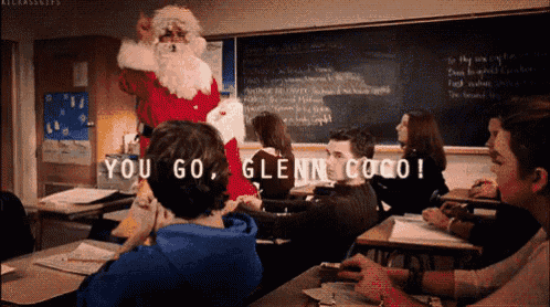 a man dressed as santa claus stands in front of a group of students in a classroom and says you go glenn coco