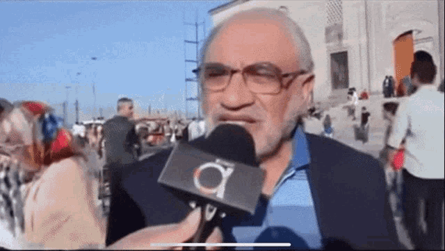a man with glasses and a beard is talking into a microphone that has the letter a on it