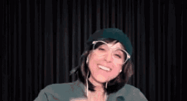 a woman wearing a green hat , glasses , and headphones is making a funny face .