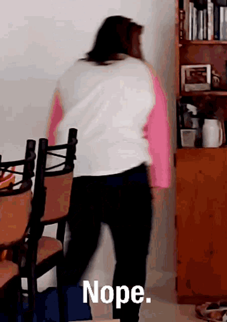 a woman in a pink and white shirt is standing in front of a bookshelf with the word nope written on it