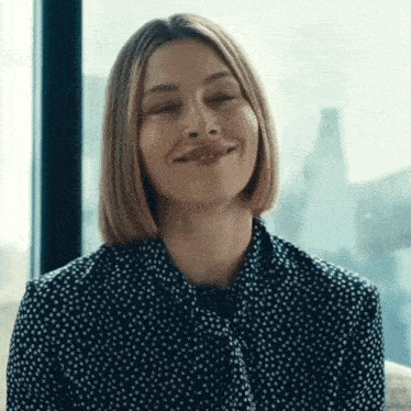 a woman is smiling with her eyes closed and wearing a polka dot shirt .
