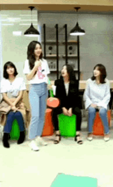 a group of women are sitting on green ottomans and one woman is standing