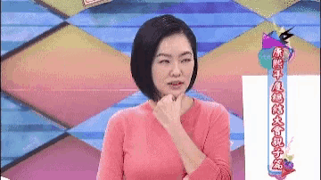 a woman in a pink shirt is sitting in front of a colorful background and making a funny face .