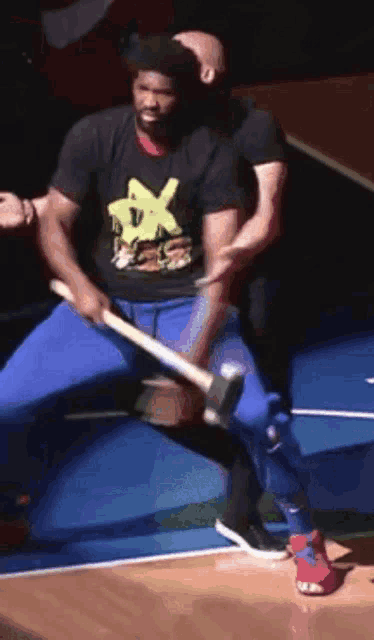 a man wearing a black shirt with the letter x on it is holding a hammer