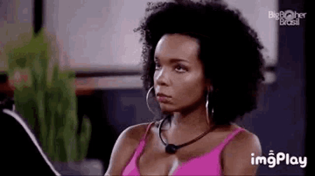a woman with curly hair and hoop earrings is wearing a pink top .