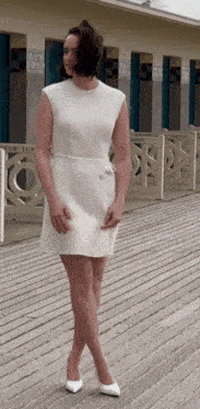 a woman in a white dress is standing on a boardwalk in front of a building that says " toilettes "