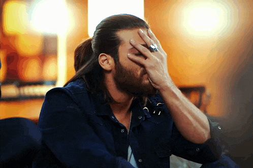 a man with long hair and a beard is covering his face with his hands