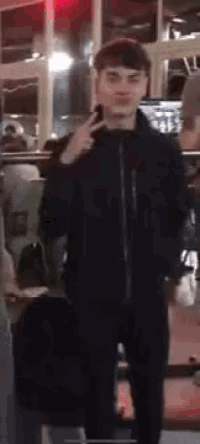 a man in a black jacket is making a peace sign with his finger .