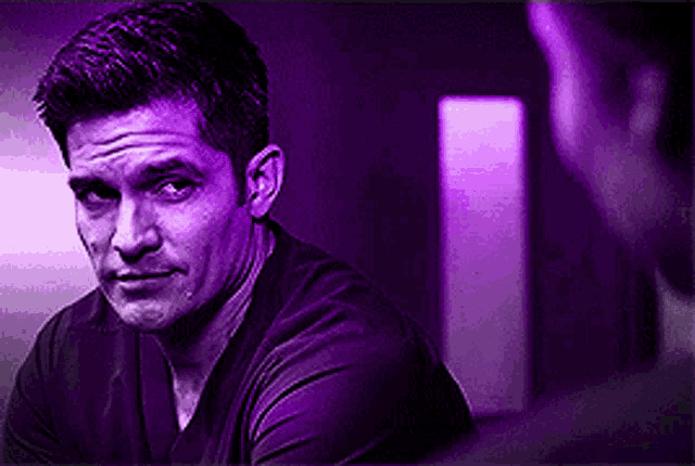 a man in a purple shirt is looking at another man in a purple light .