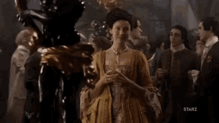 a woman in a yellow dress is standing in front of a crowd of people in a room .