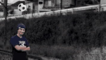 a man in a blue shirt is standing with his arms crossed in front of a wall .