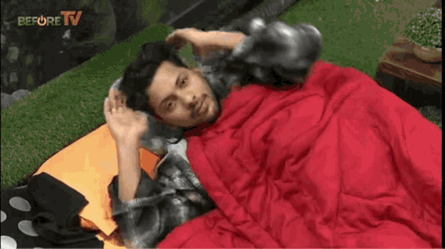 a man is laying under a red blanket with the words before tv behind him .