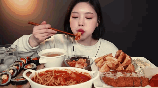 a woman is eating noodles with chopsticks while sitting at a table full of food