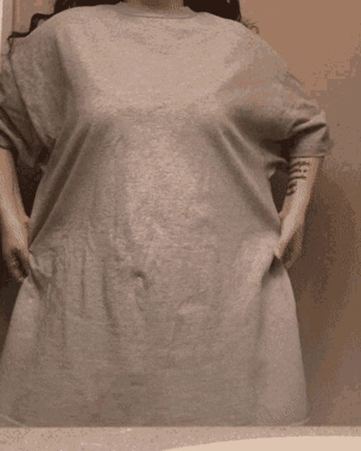 a woman with a tattoo on her arm is standing in front of a mirror wearing a grey shirt