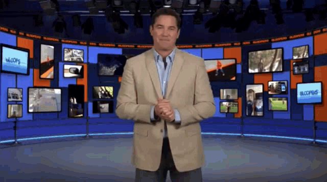 a man in a suit stands in front of a wall of television screens including one that says " bloom "