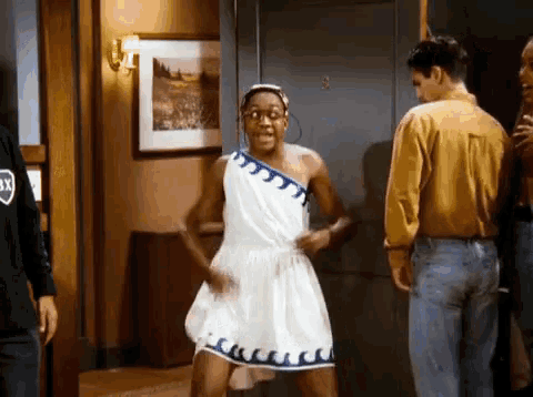 a woman in a white dress is dancing in a hallway while a man stands behind her .