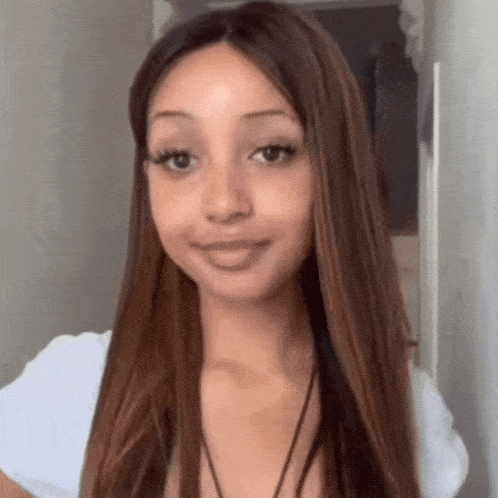 a woman with long brown hair is wearing a white shirt and a black necklace .