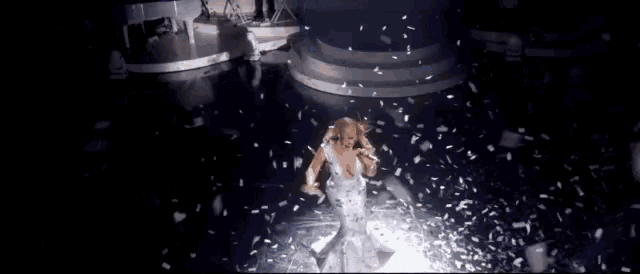 a woman in a white dress is standing on a stage with confetti falling around her