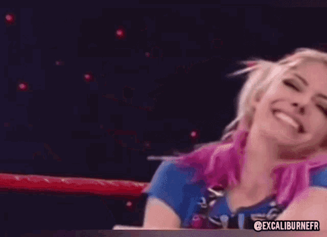 a woman with pink hair is sitting in a ring and smiling .