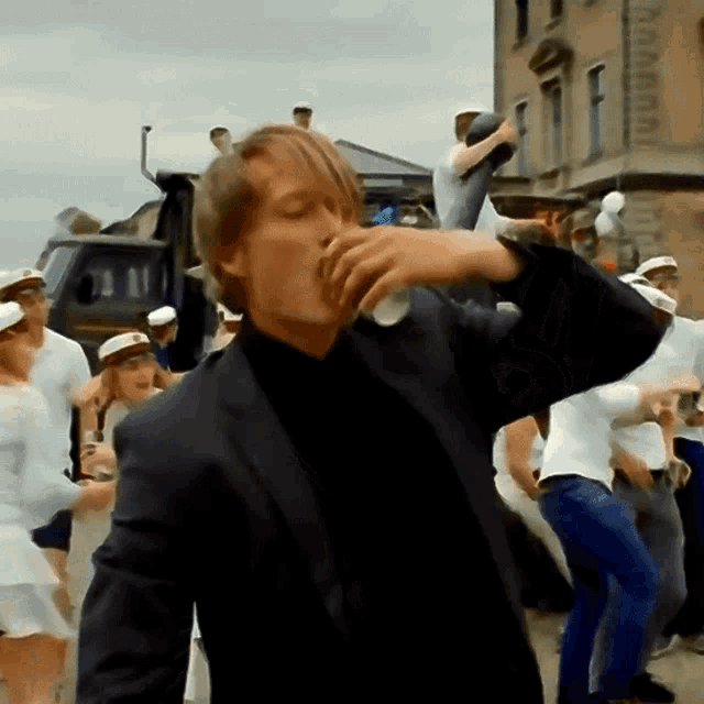 a man in a suit is drinking from a glass in front of a group of people