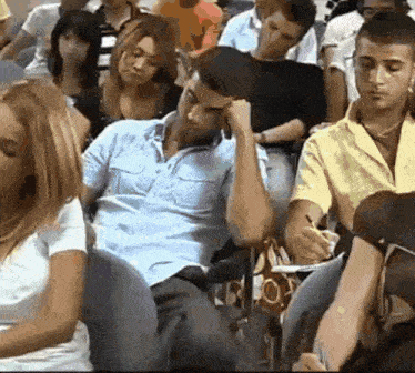 a group of people are sitting in a classroom with one man sleeping on the floor
