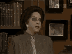 a woman wearing sunglasses is sitting in front of a bookshelf .