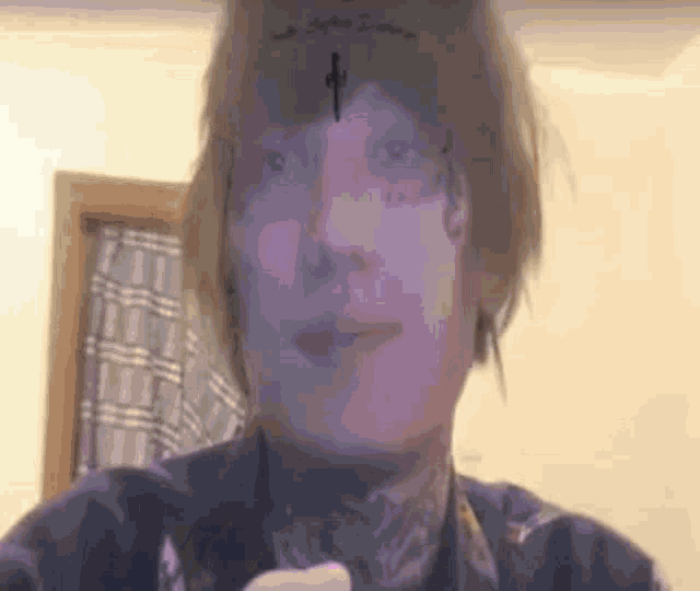 a man with a cross tattoo on his forehead is taking a selfie .