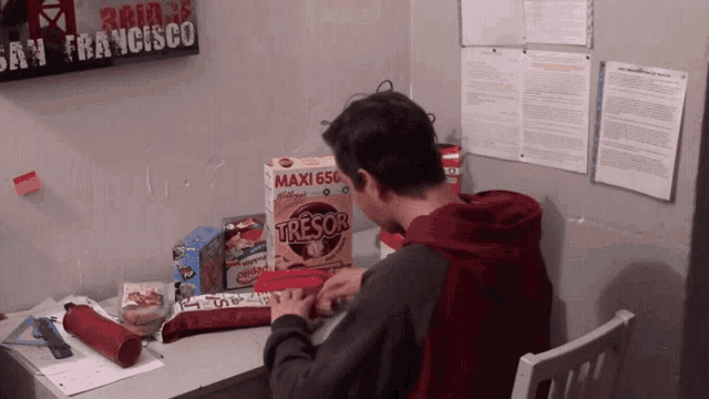 a man sits at a desk with a box of tresor cereal on it