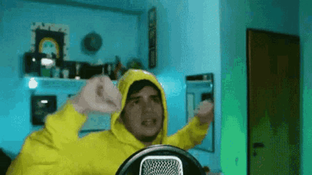 a man in a yellow hoodie is sitting in front of a microphone