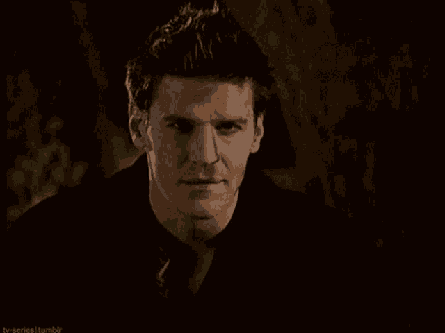 a man in a black shirt is smiling and looking at the camera in a dark room .
