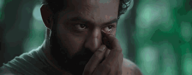a man with a beard is covering his face with his hand .