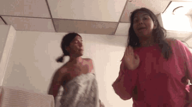 two girls are wrapped in towels and dancing in a bathroom .