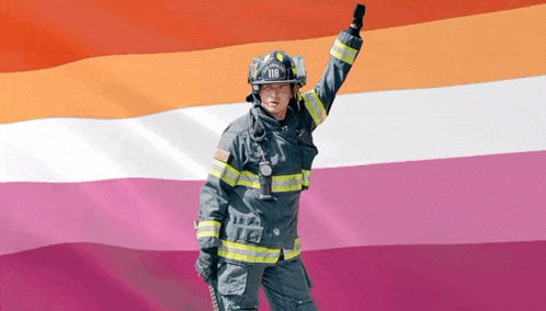 a fireman with the number 118 on his helmet is holding up his hand in front of a lesbian flag .