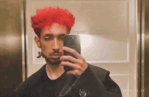 a man with red hair is taking a selfie in an elevator with his phone .