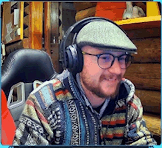 a man wearing headphones and a hat is smiling in front of a log cabin