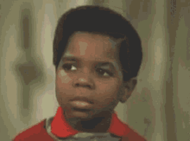 a young boy in a red shirt is making a funny face and asking what you talkin bout ?