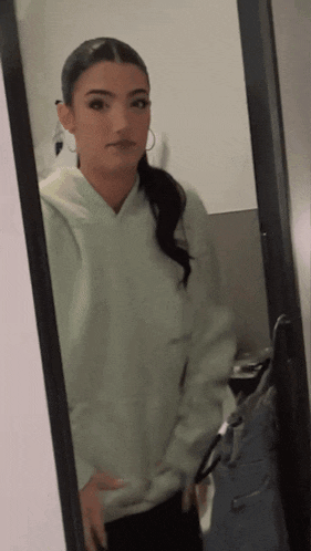 a woman is taking a selfie in front of a mirror while wearing a white hoodie
