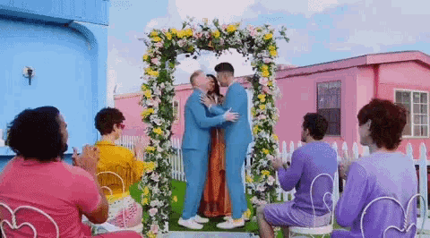 a man and woman are kissing under a flower arch while a group of people watch .