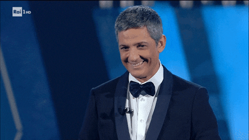 a man in a tuxedo is smiling and waving in front of a rai hd sign